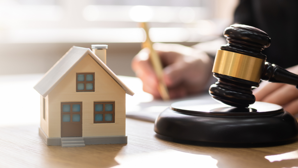 A person writing on a table with miniature house and a gavel
