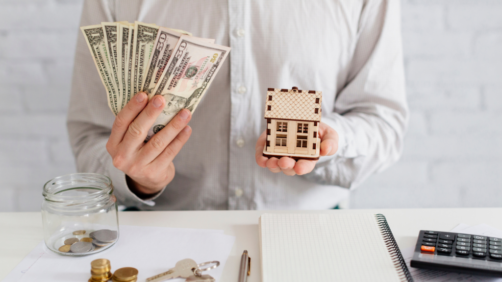 A person holding a miniature house and money