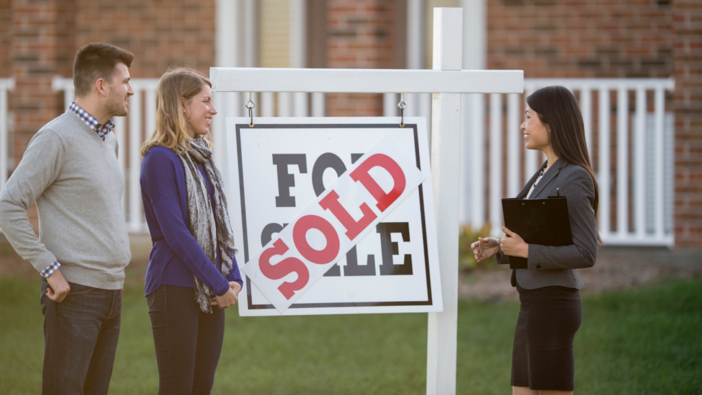 A couple and an agent standing in front of a house with a SOLD sign